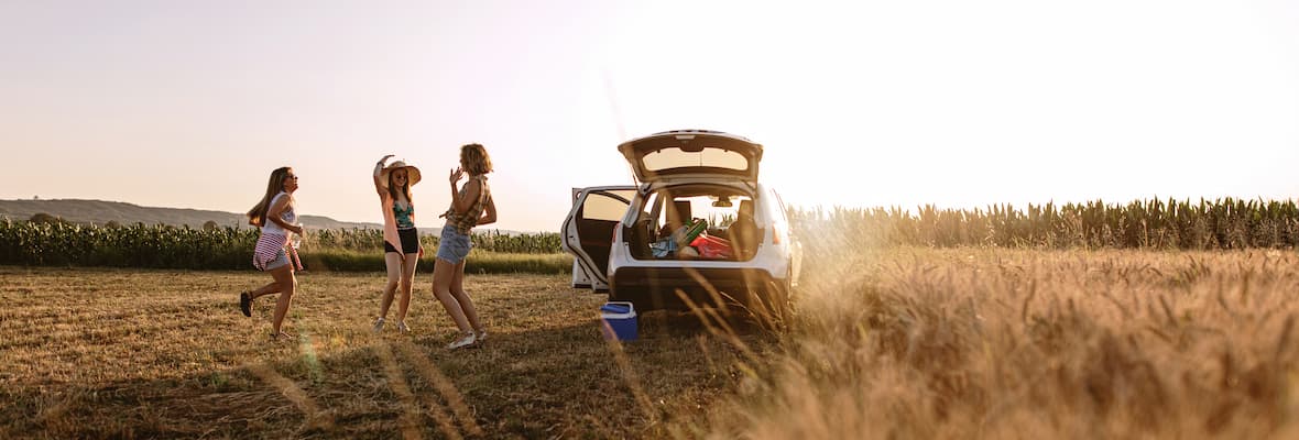 group of girl friends standing next to packed car at sunset in field