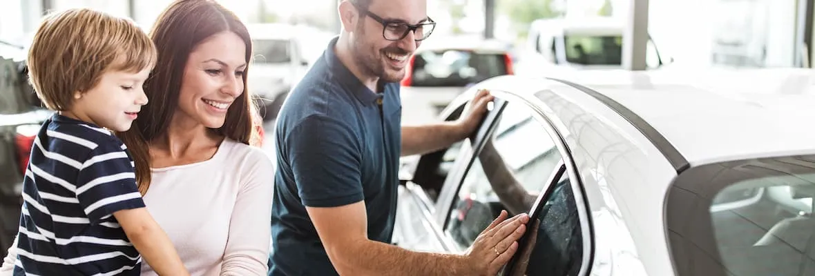 A young family with a child in their arms happily looks at a new vehicle to purchase.