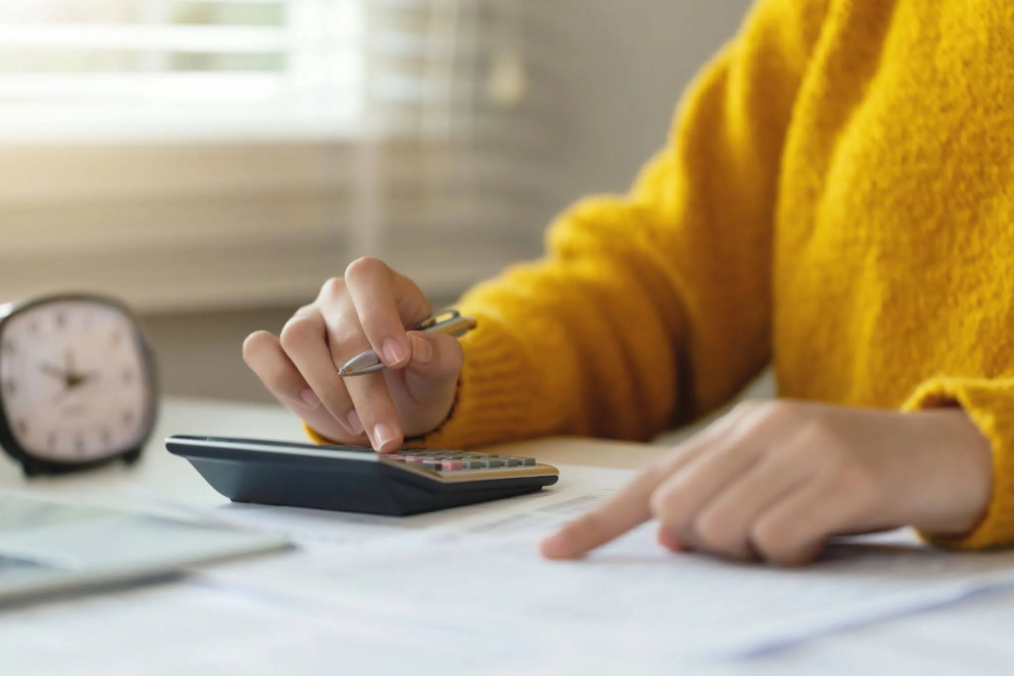 A woman in a yellow jumper does tax calculations at a desk with a calculator