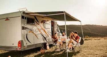 Two couples laughing around table in front of caravan at sunset