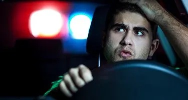 A concerned man looking sitting in the driver's seat at the rearview mirror at the police lights.