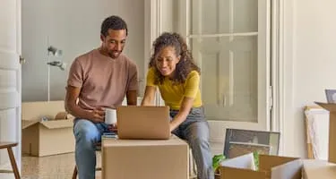 Man and woman looking at laptop surrounded by moving boxes
