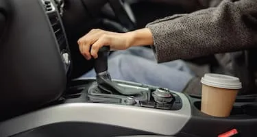 A woman changes speed by moving the leather gear selector forward in her car.