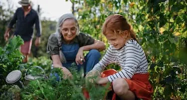 Grandmother smiles at her granddaughter as they both work in a vegetable patch.