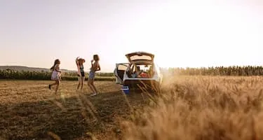 Group of girl friends standing next to packed car at sunset in field