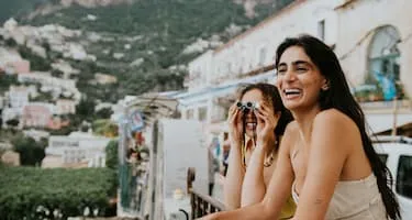 Two young women use binoculars off a balcony in Positano