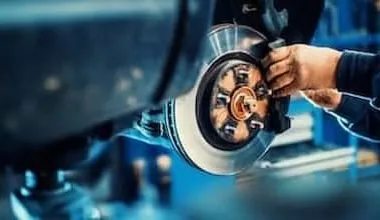 A mechanic replaces car brake pads on a car that was lifted to eye level using a hydraulic jack.