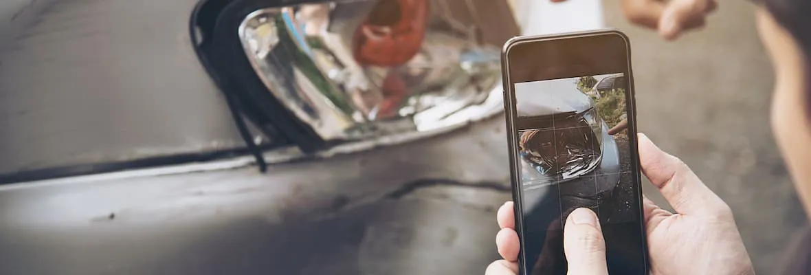 Smartphone photographing a dented car bumper