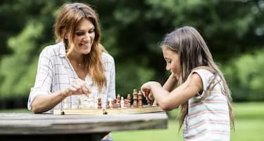 Mother and daughter play chess in the park 