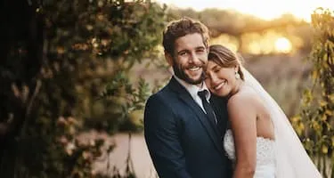 Newlyweds smiling for wedding photoshoot during golden hour in an orchard.