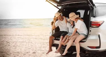 mum dad and daughter sitting in boot of car parked on beach