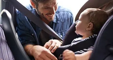Young man smiles as he is strapping a baby into a car seat