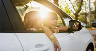 two children hanging out window of white car smiling