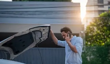 Man looks underneath the bonnet of his car while talking on his mobile phone.