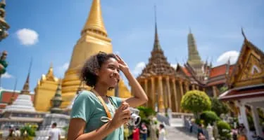 Young woman holds a camera as she walks past the Wat Phra Kaew temple in Bangkok, Thailand. 