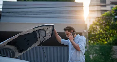 Man looks underneath the bonnet of his car while talking on his mobile phone.