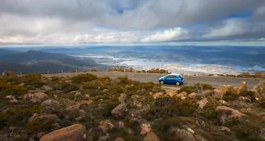 A small blue car drives on top of Mount Wellington above Tasmania's capital city, Hobart.