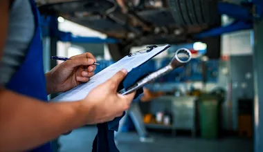 A mechanic holds a car servicing checklist and is marking off work completed