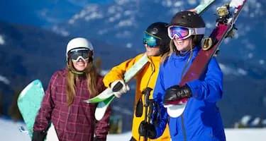 A group of happy friends carry snowboards and skis up a mountain