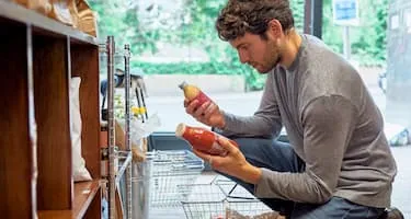 man grocery shopping kneeling down comparing different food products
