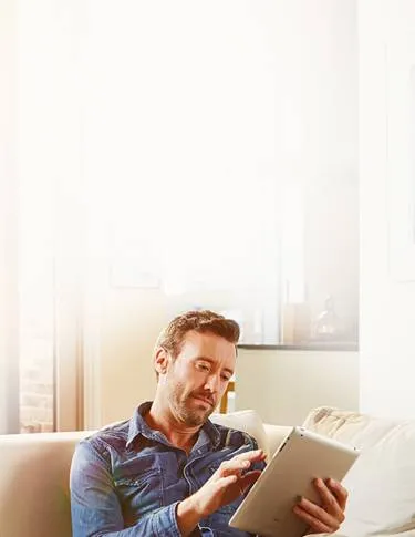Man sitting on the couch interacting with their tablet.