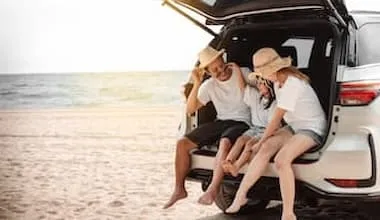 mum dad and daughter sitting in boot of car parked on beach