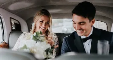Bride and groom smiling in the backseat of a car