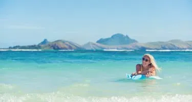 Young woman lies on a pool toy in the ocean on a beach in Fiji