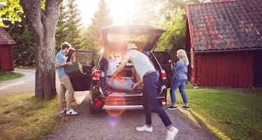 Four friends loading luggage into car on road on sunny day