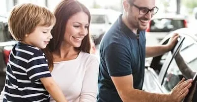 A young family with a child in their arms happily looks at a new vehicle to purchase.