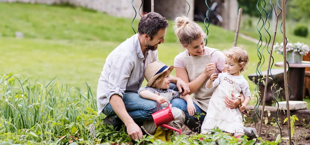 Man and woman with two young children who have mud on their hands and faces tending to a backyard vegetable patch.