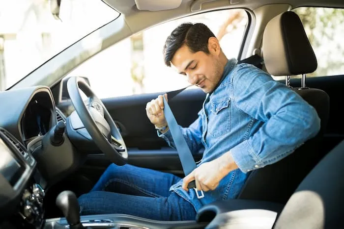 A man buckles his seatbelt in the front seat before he starts driving his car.
