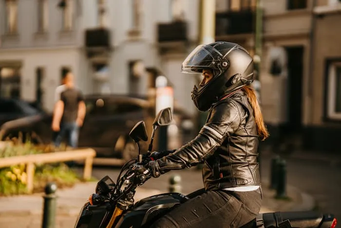 A female motorcyclist wearing a motorcycle helmet, jacket and gloves rides through the city.