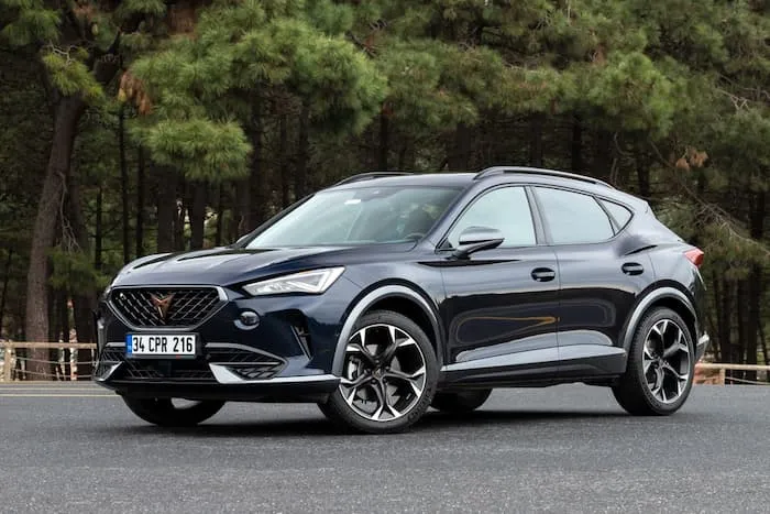 Black Cupra Formentor Hybrid is parked on concrete in front of tall green trees