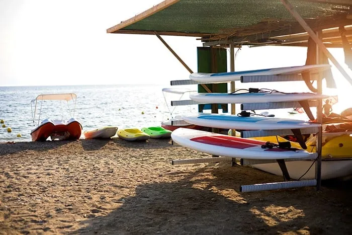 Jet skis and paddleboards stored beside a beach at sunset.