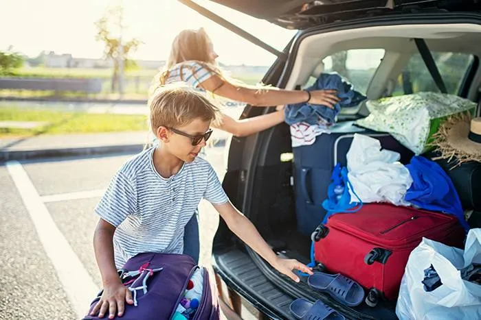 Child assisting with packing car for beach trip.