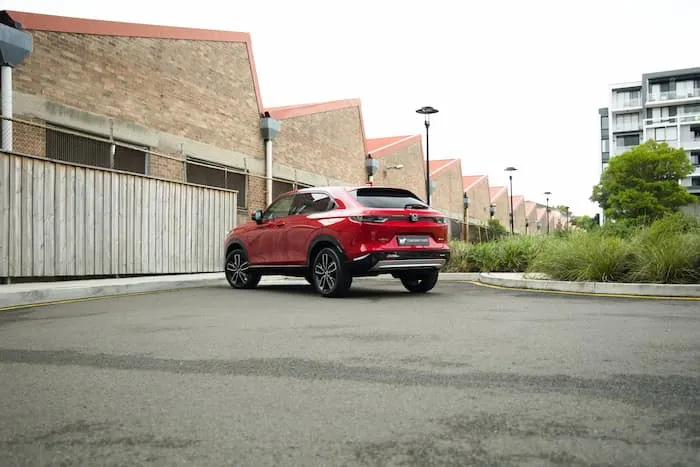 red Honda HR-V parked in car park facing fence in front of houses