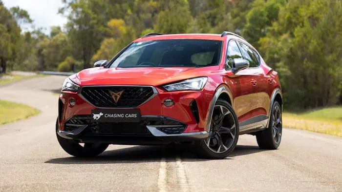 Red Cupra Formentor VZ is parked in the middle of a road surrounded by trees