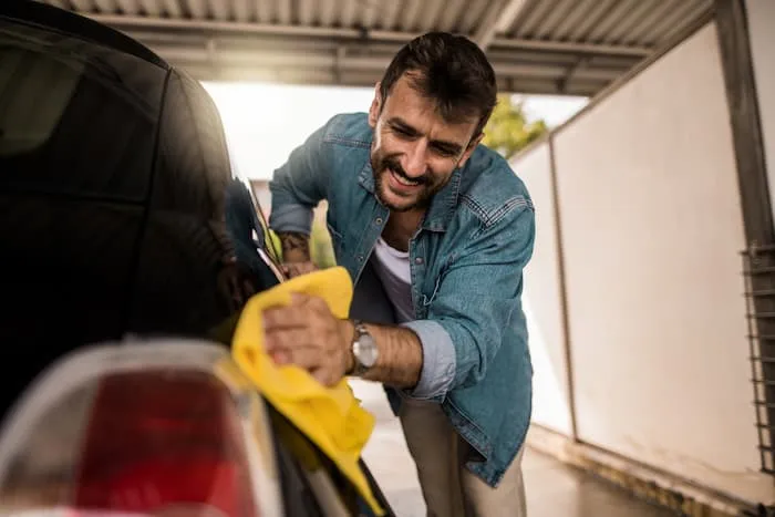 A man wipes down the side of his car with a yellow microfibre cloth in his garage.