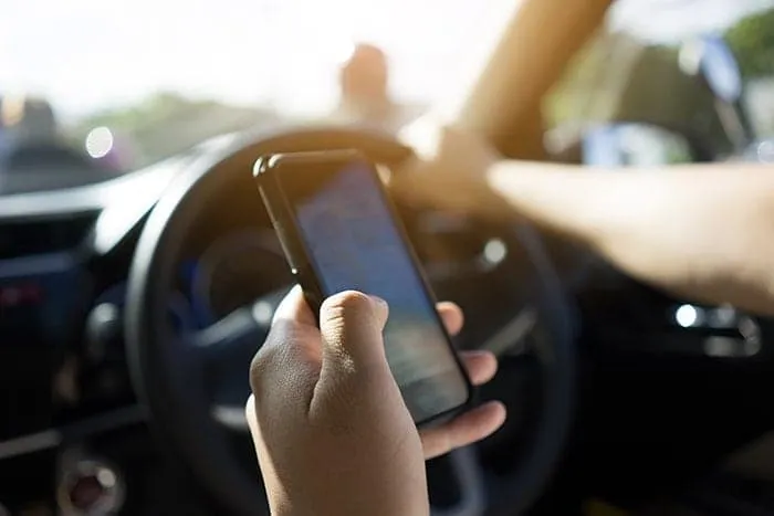 Person looking at mobile phone while in car drivers seat with other hand on steering wheel