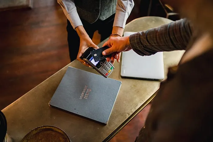 A guest taps a payment card on a terminal at a hotel counter.