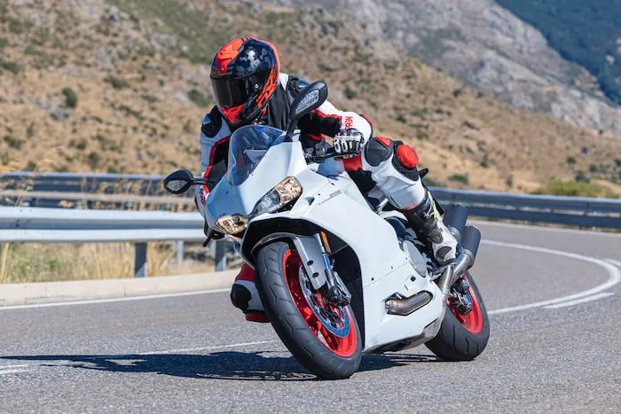 A rider leans on a sports bike around a road corner while wearing full protective gear.