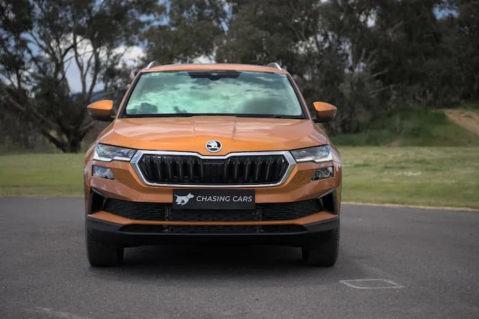 Orange Skoda Karoq Style parked in front tall trees and green grass