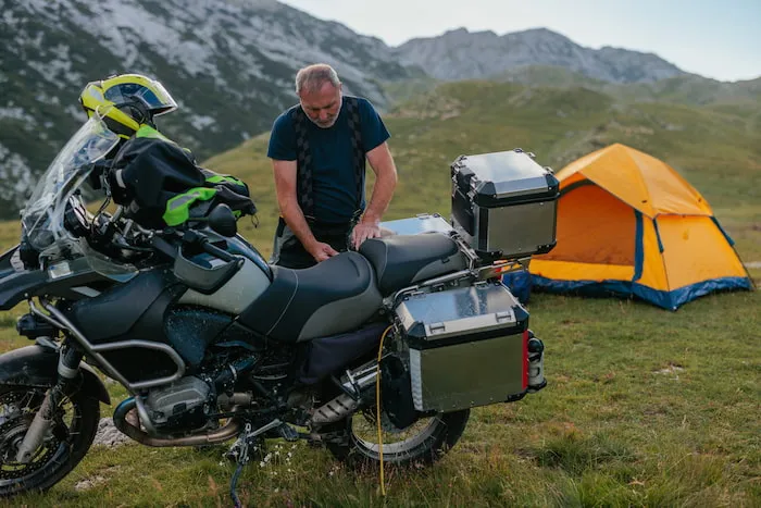 A man is camping and unpacking gear from his touring motorcycle luggage compartment in the mountains.
