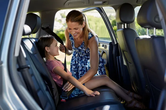 Mother or guardian secures her young daughter with seat belt into backseat of car