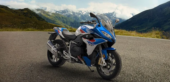 A sleek sport touring motorcycle stands alone on a road in front of snowy mountain peaks.