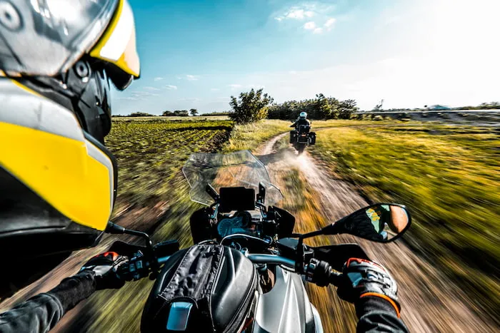 An adventure motorcyclist speeding up on a country road with his friend on a sunny day.
