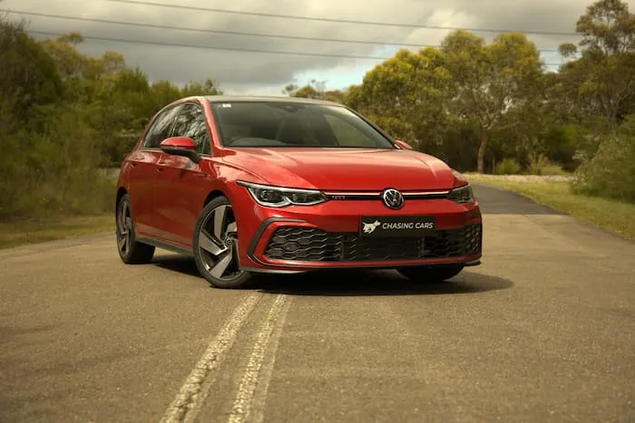 red volkswagen golf parked across white lines on road in front of cloudy sky