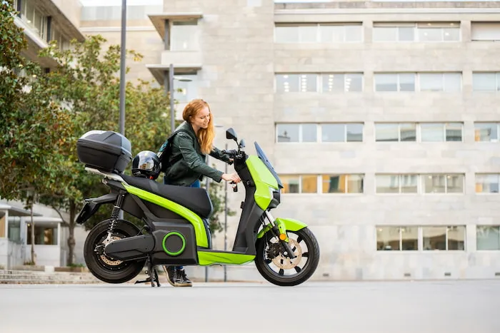 A woman puts her keys into her green electric motorcycle parked on the street.
