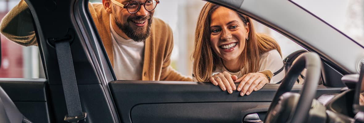  A couple peers into a car from the passenger side window looking excited.